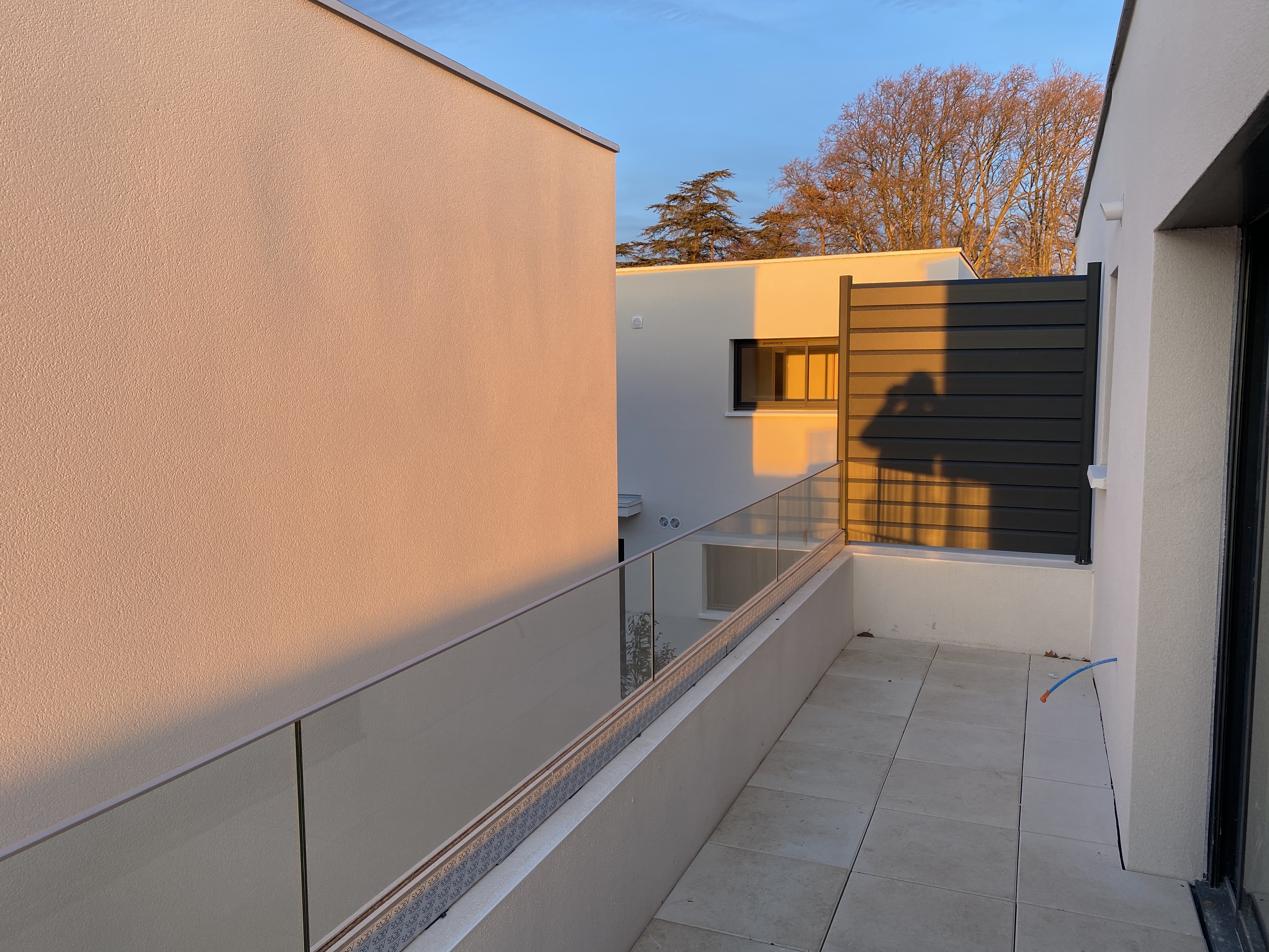 terrasse d'une maison individuelle sécurisé par un garde corps en verre appliqué sur un muret.