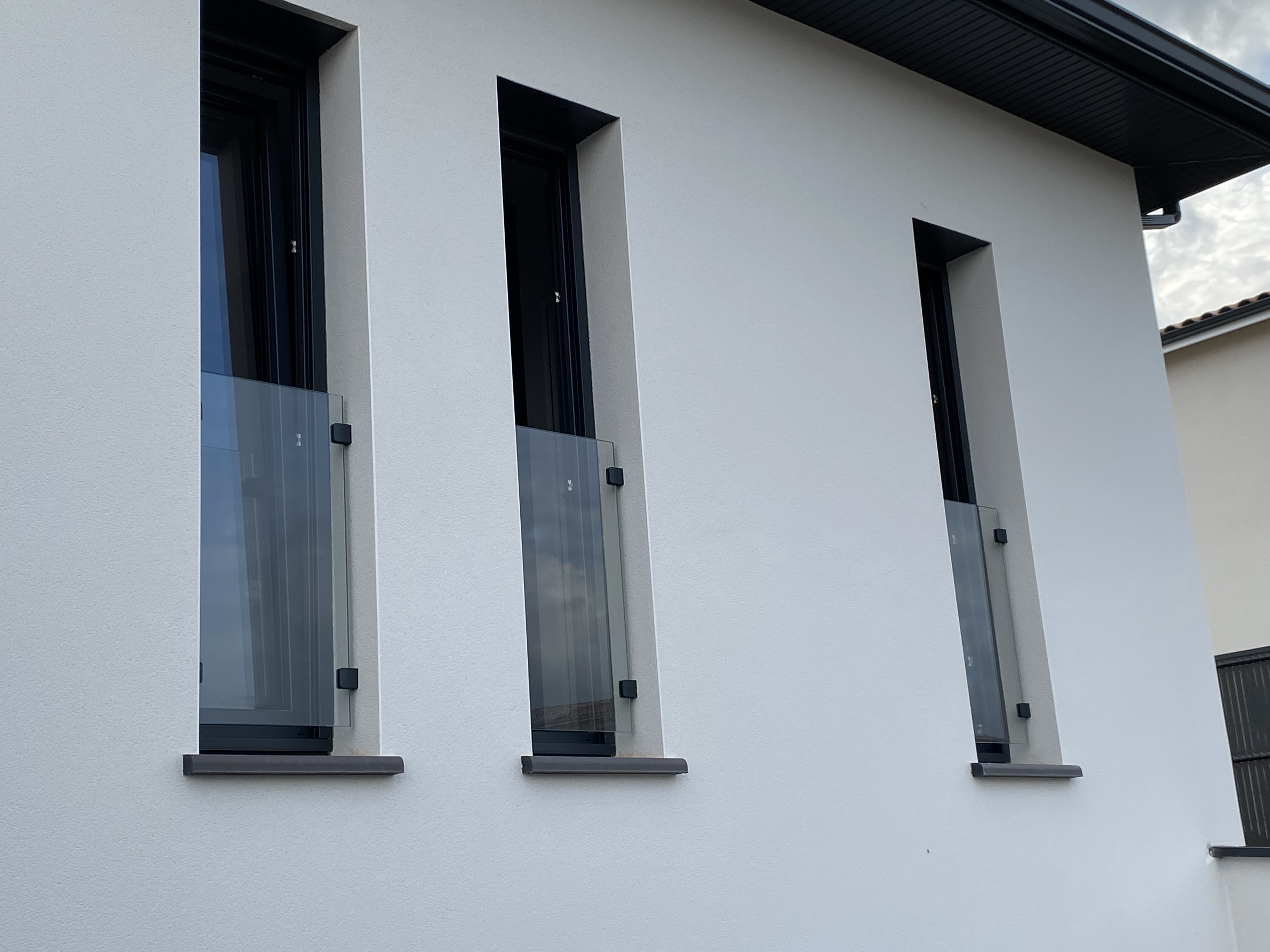 Rangée chic de trois garde-corps de fenêtres en verre fixés avec des pinces thermolaquées gris anthracite, à Toulouse entre Foix et Moissac.