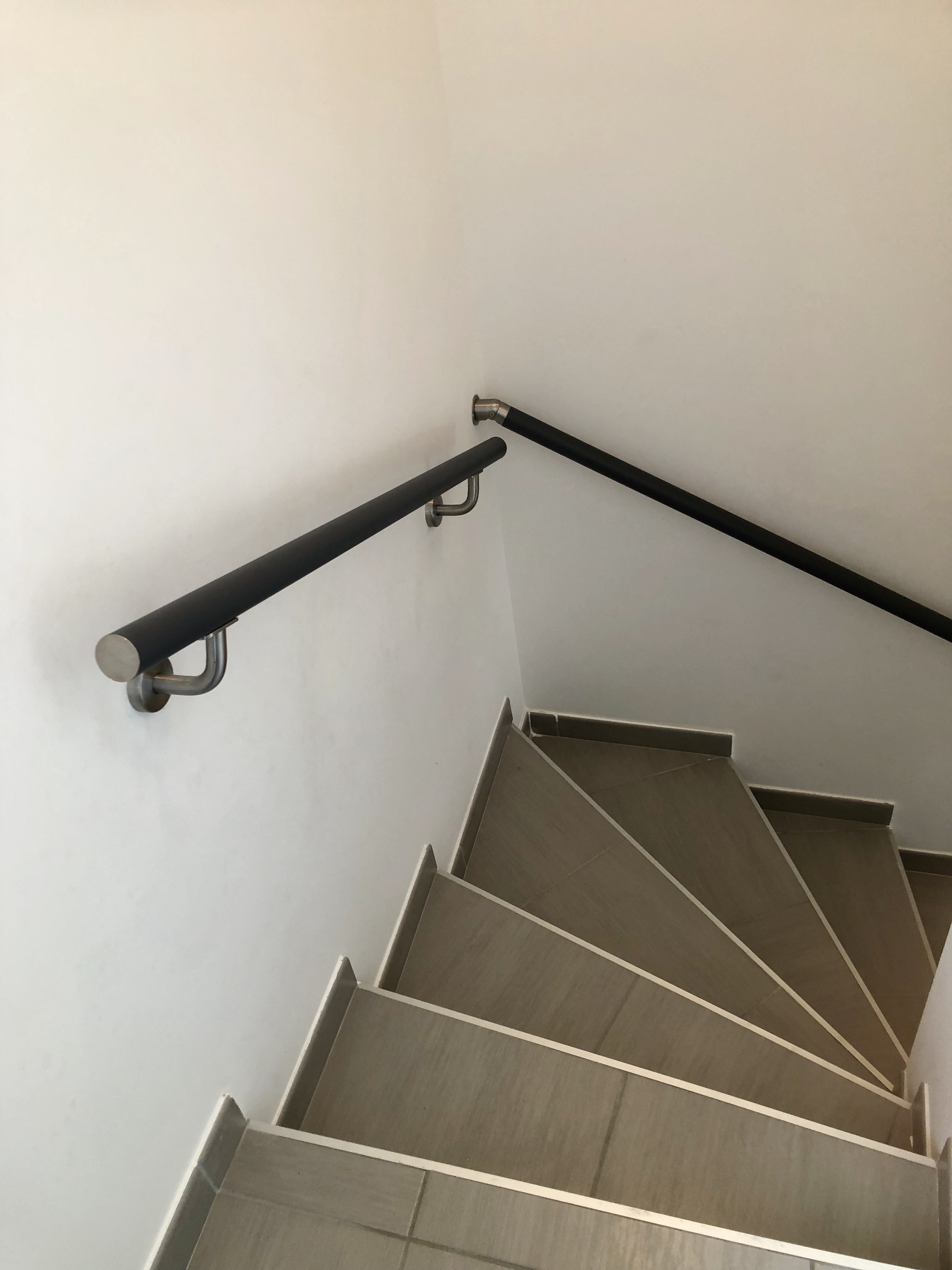 Main courante le long d'un mur, thermolaquée en noir 2100, sur un escalier, dans le département de l'Hérault.