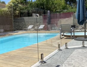 Agréable vue sur une piscine sécurisée par une barrière en verre fixée avec des pinces en inox, en région Occitanie.