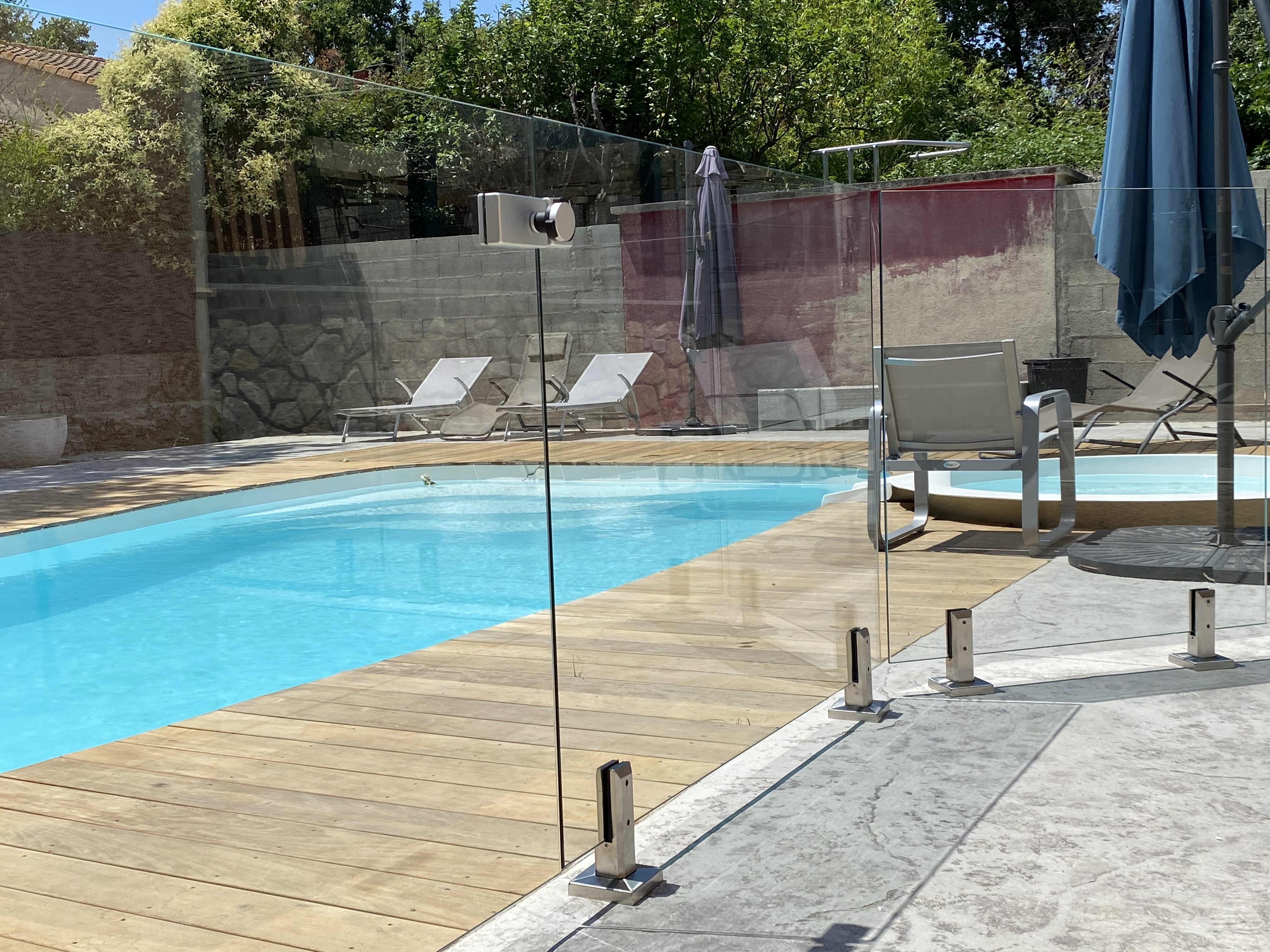Agréable vue sur une piscine sécurisée par une barrière en verre fixée avec des pinces en inox, en région Occitanie.